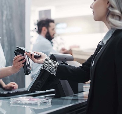 Attractiveness of modern contactless, automated, and individualized shopping for customers Blonde customer in black blazer pays contactless with her smartphone at the checkout of a modern store